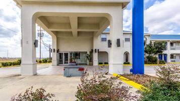A building with a covered entrance, a blue pillar, and a parking area with a yellow line.