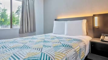 Habitació d'hotel amb llit, una taula de nit, un telèfon i una finestra amb cortines.