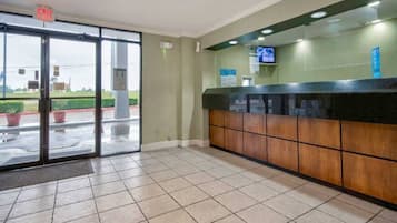 Zona de recepció amb entrada per porta de vidre, taulell de recepció i televisió penjada a la paret.