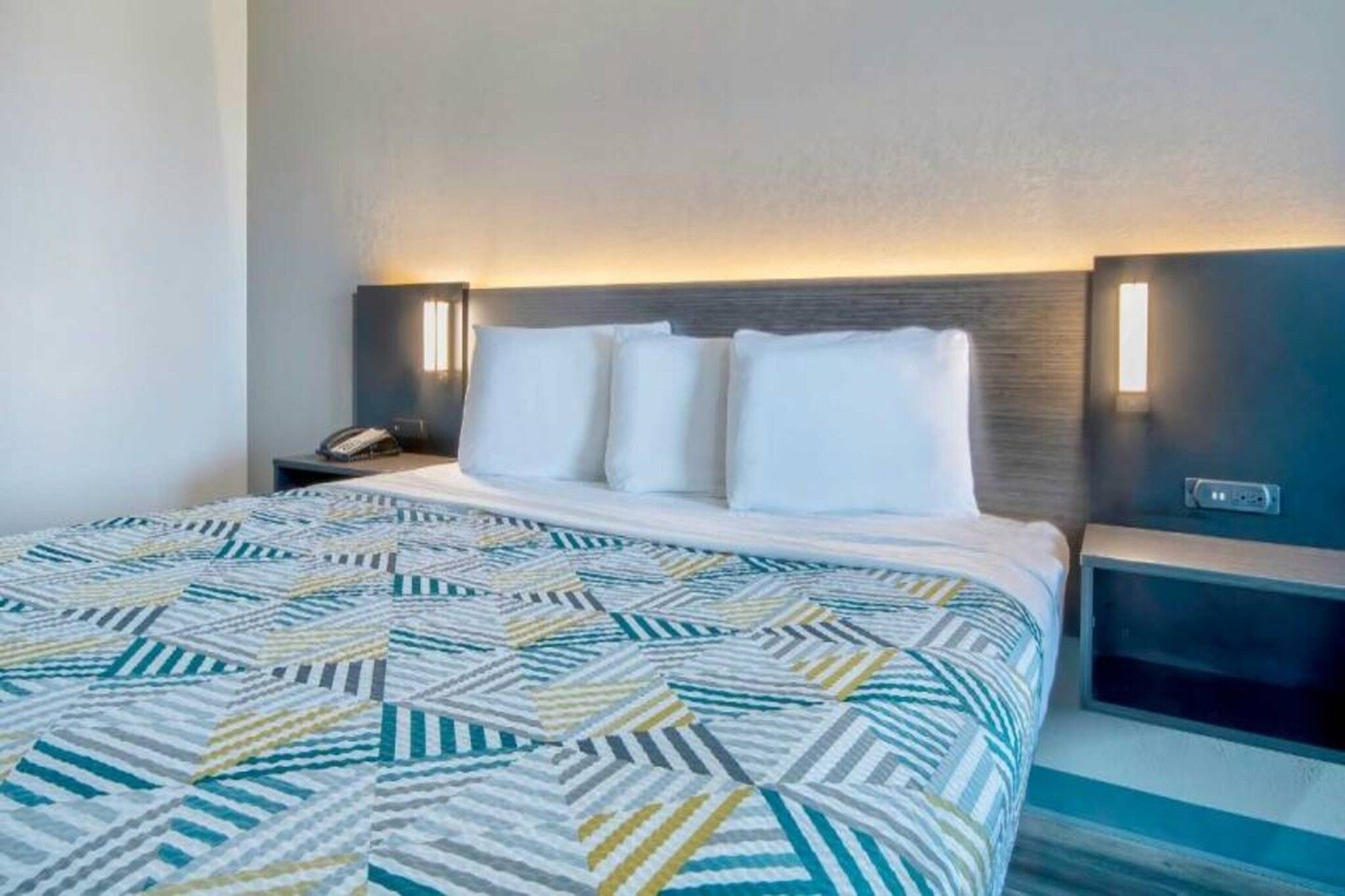 A hotel room with a bed, a nightstand, and a wall-mounted lamp.