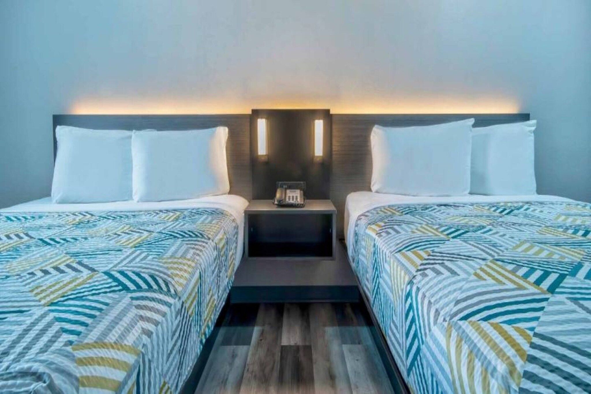 A hotel room with two beds, a nightstand, and a wall-mounted light fixture.