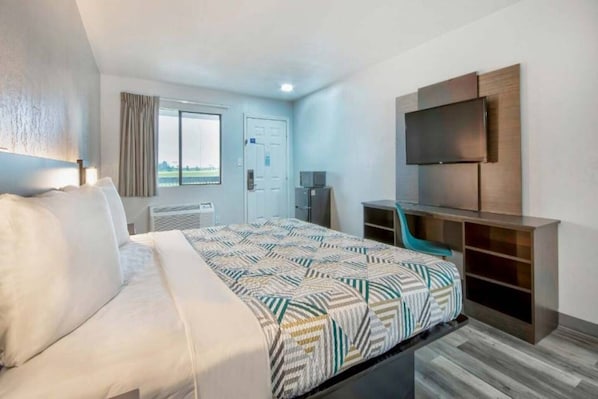 Una habitació d'hotel amb llit, escriptori, cadira, televisió i finestra.