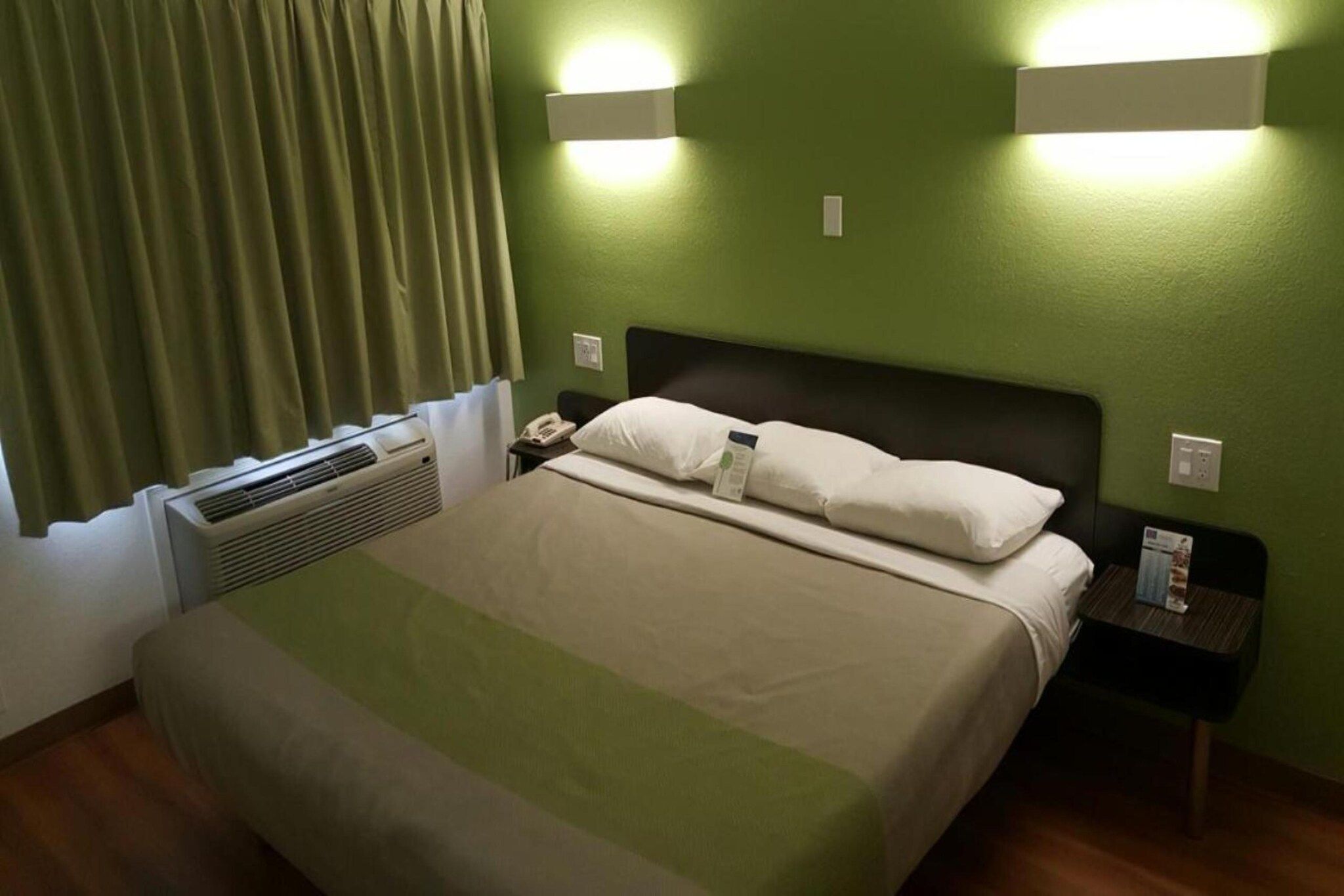 Una camera d'albergo con un letto, un comodino, un telefono e una lampada a parete.