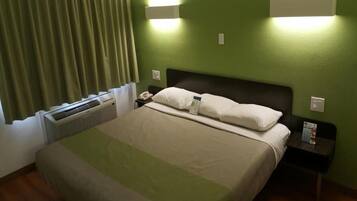Una camera d'albergo con un letto, un comodino, un telefono e una lampada a parete.