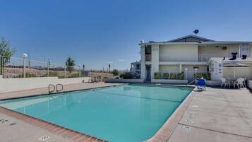 A swimming pool with a clear blue water, a white building with a balcony, and a fenced area with outdoor seating.