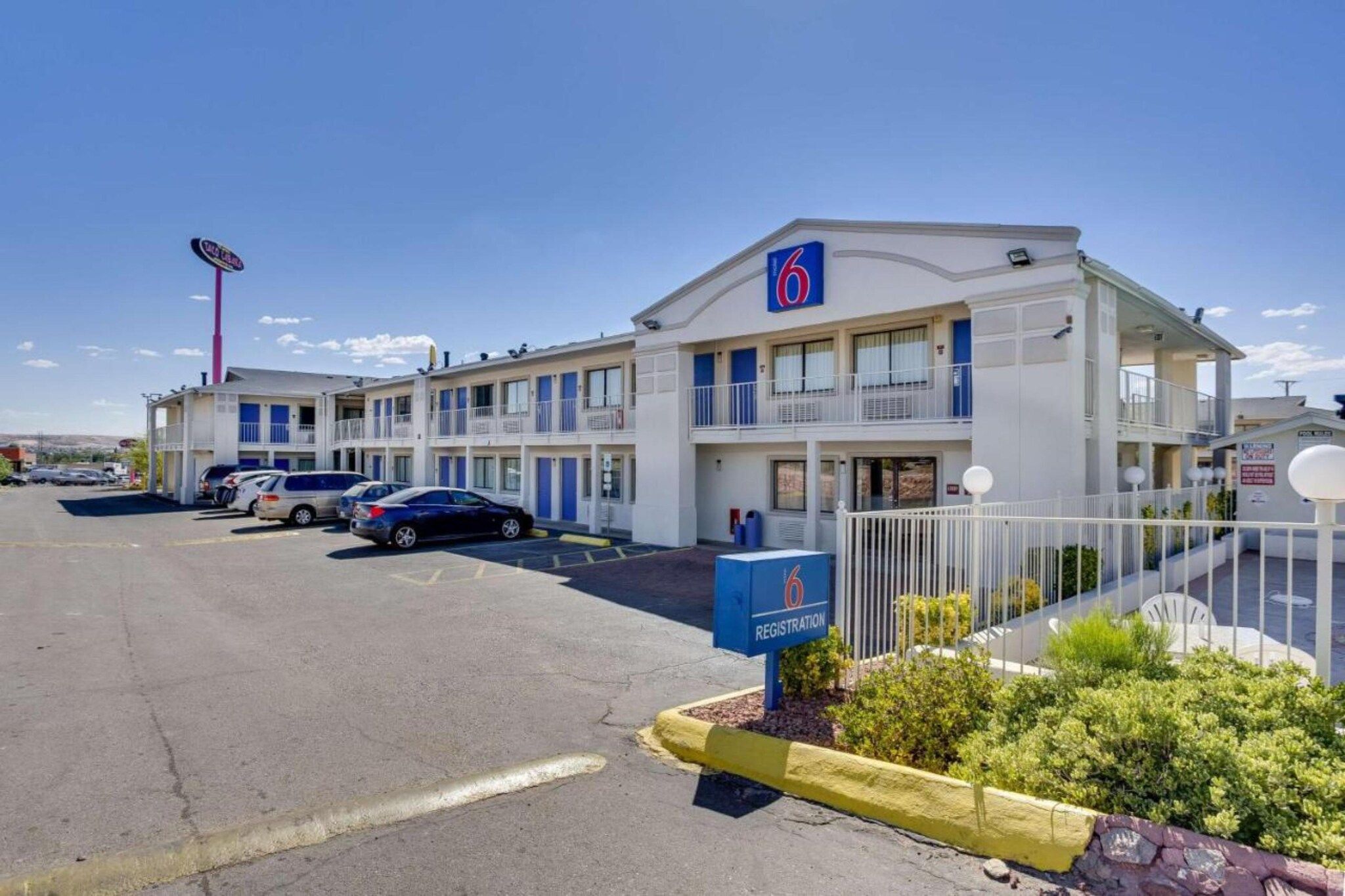 A motel with a registration box, multiple parking spaces, and a fenced parking area.