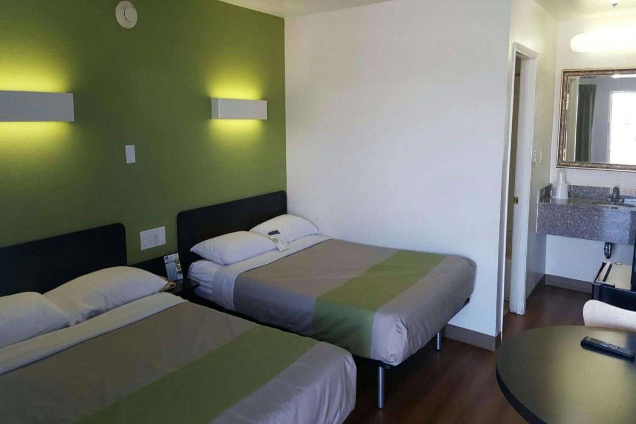 Una camera d'albergo con due letti, un tavolino e un bagno con uno specchio.