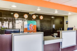 A hotel reception desk with a sign for a 6 Motel, clocks indicating different time zones, and a computer on the desk. - 2 FULL BEDS | NON-SMOKING (El Paso TX)