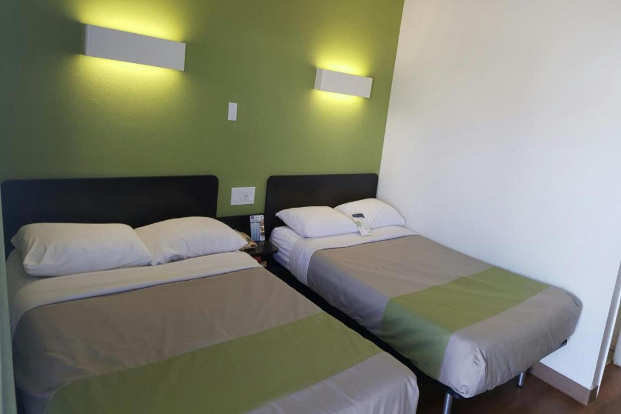 Une chambre avec deux lits simples, chacun étant équipé d’un oreiller et d’une couverture. Des appliques murales sont fixées aux murs verts.