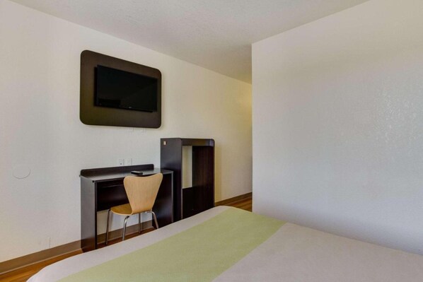 Een hotelkamer met een bed, een bureau, een stoel en een aan de muur bevestigde televisie.