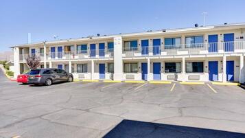A motel with a two-story structure, a parking lot, and a red car parked in the foreground.
