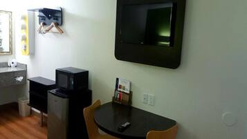Une pièce compacte comprenant un coin cuisine, un téléviseur à écran plat fixé au mur, une petite table avec deux chaises et une poubelle.