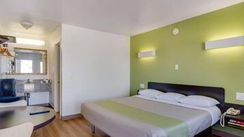 A hotel room with a bed, bedside table, and a desk with a chair.
