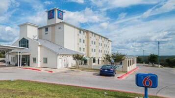 A multi-story hotel with a prominent '6' sign, a covered entrance, and a parking area.