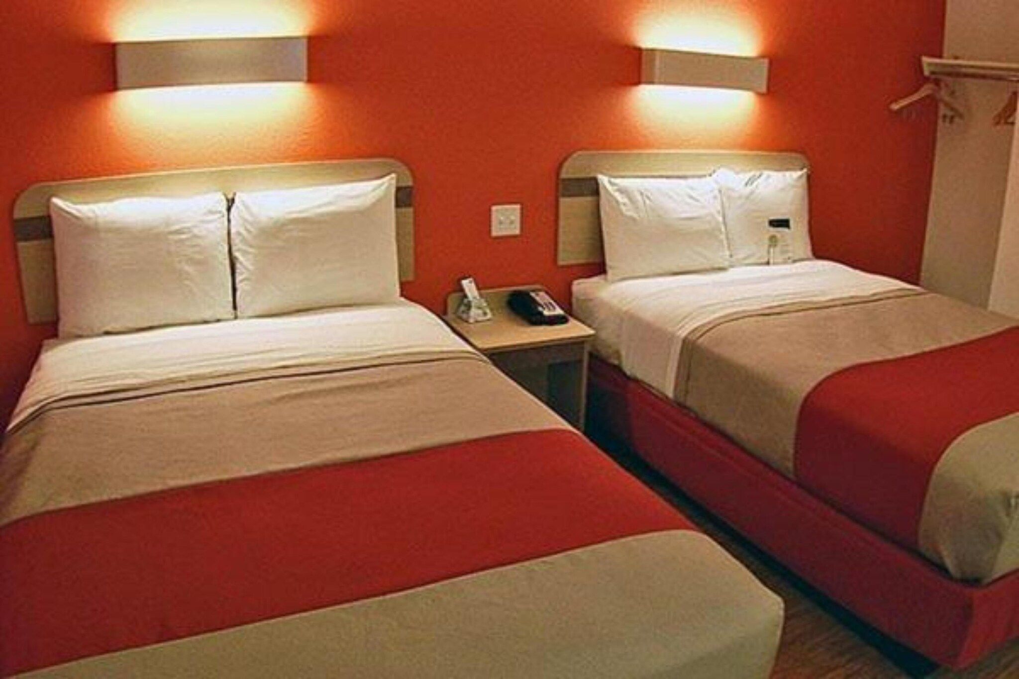 Een hotelkamer met twee enkele bedden, elk voorzien van een hoofdeinde, een nachtkastje met een telefoon, en een wandlamp.