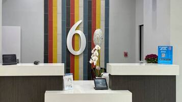 A reception desk with a large number '6' on the wall, a small potted plant, and a blue informational sign.
