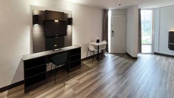 Un salon moderne doté d’un téléviseur à écran plat fixé au mur, d’un coin repas avec une table et des chaises, et d’une grande fenêtre laissant entrer la lumière naturelle.