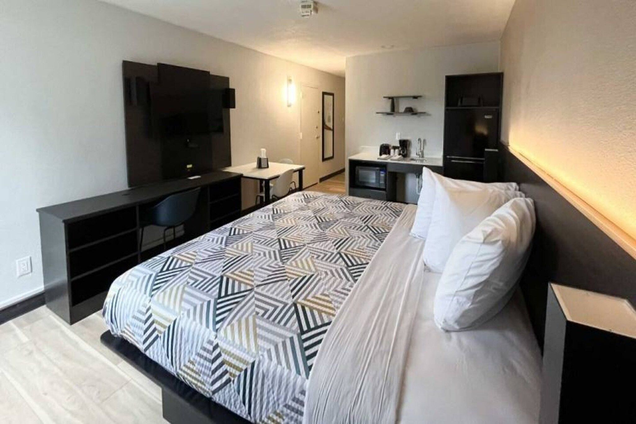 Habitación de hotel moderna con una cama grande, un escritorio, un televisor de pantalla plana y una kitchenette.