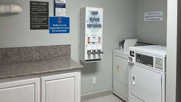 A laundry area with a sink, soap, bleach, and softeners dispenser, and a washing machine.