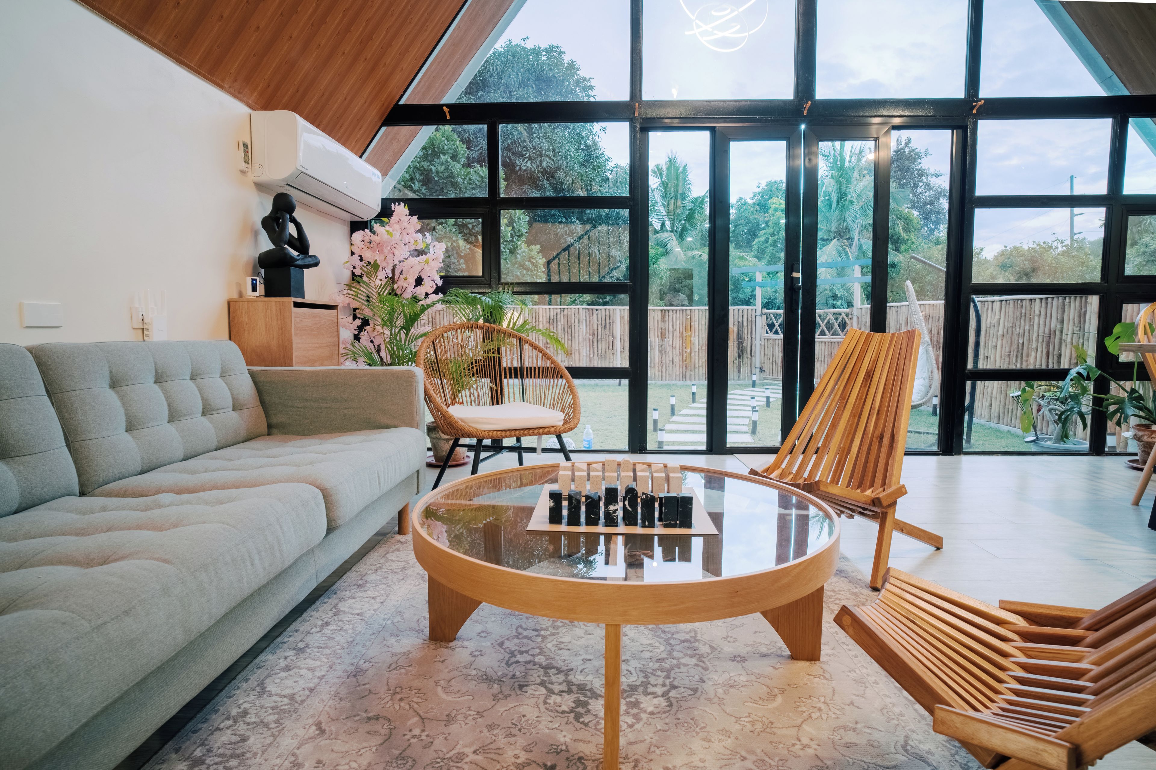 A modern living room with a sofa, a glass coffee table, and two wooden chairs.