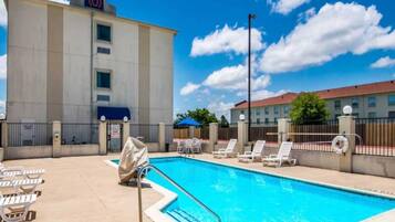 A hotel pool area with a clear blue pool, lounge chairs, and a building with a '6' sign.