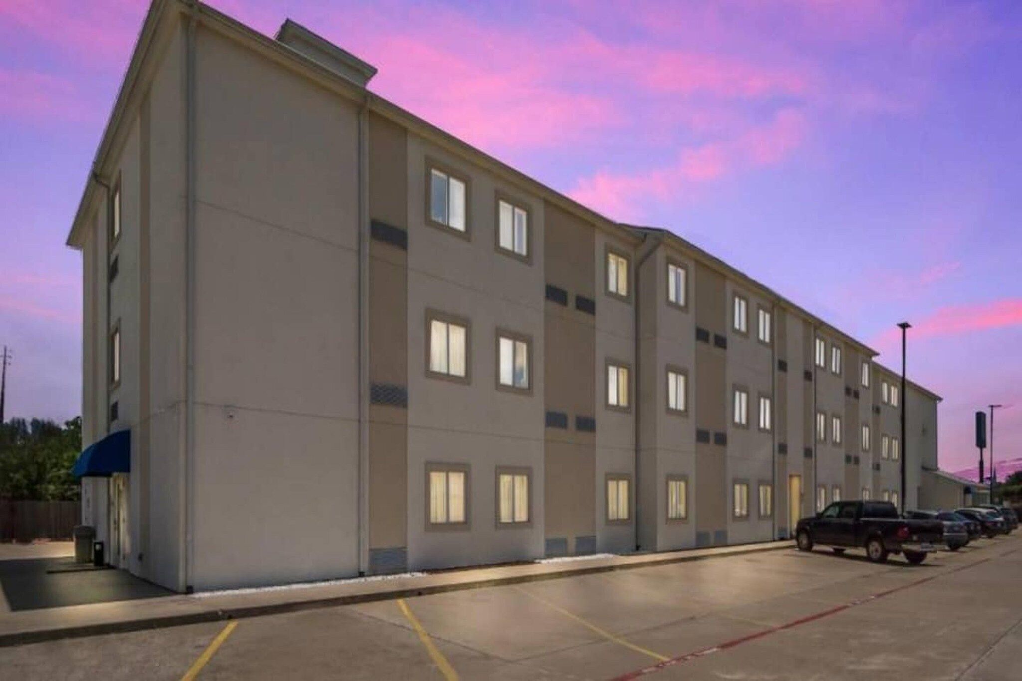 Un hotel de varios pisos con fachada plana, varias ventanas y un estacionamiento con coches.