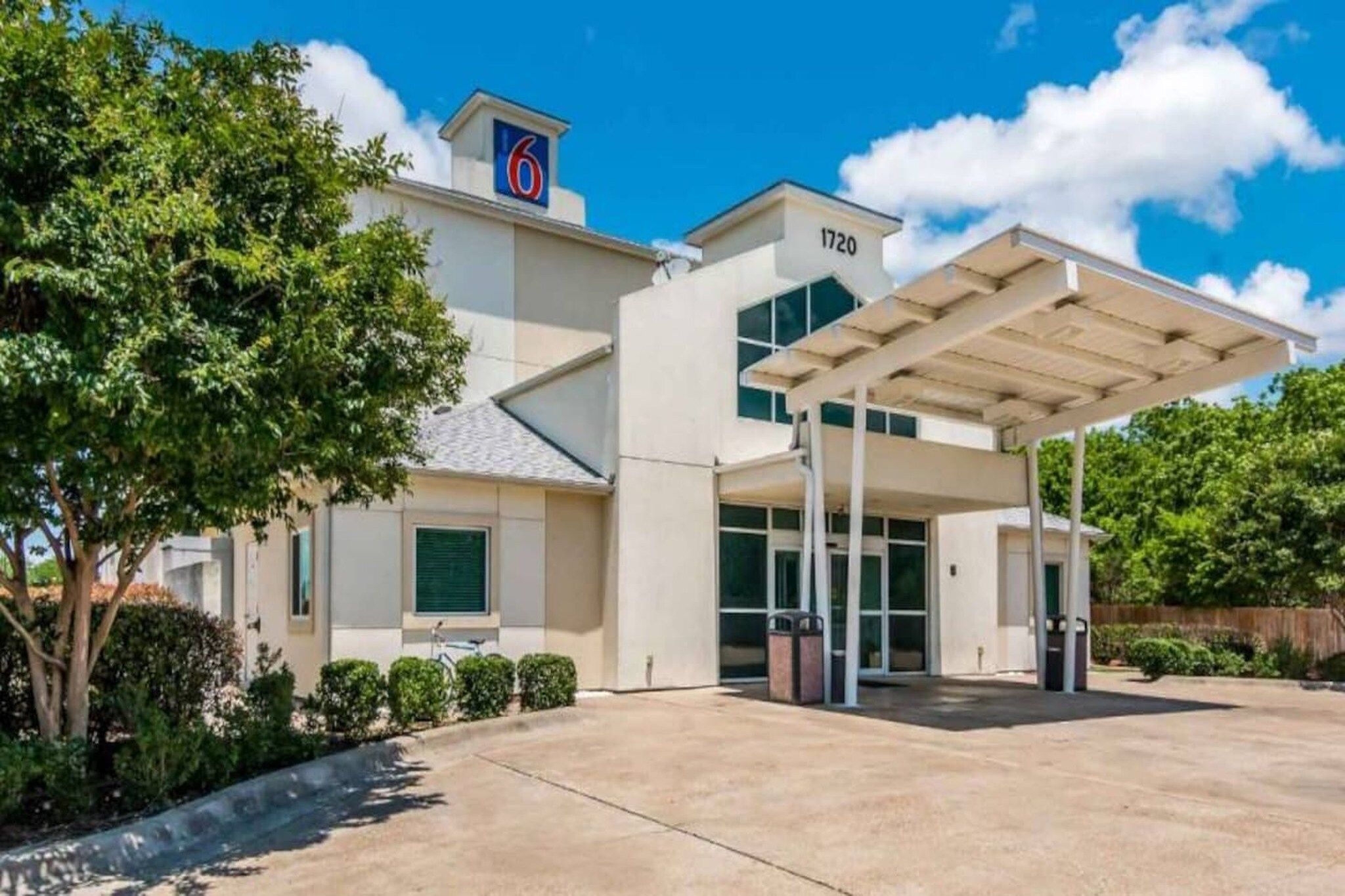 A modern hotel with a covered entrance, a prominent '6' sign, and a number '1720' on the building.