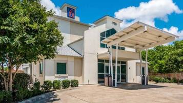 A modern hotel with a covered entrance, a prominent '6' sign, and a number '1720' on the building.