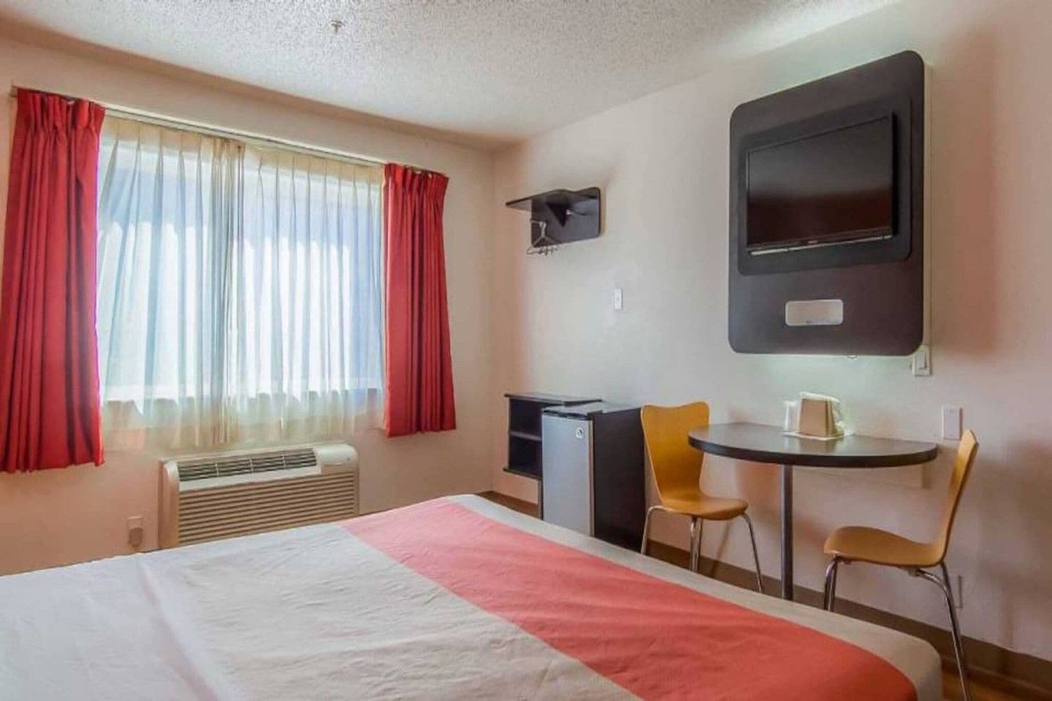 A hotel room with a bed, a desk, two chairs, a television, and a window with curtains.