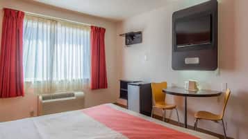 A hotel room with a bed, a desk, two chairs, a television, and a window with curtains.