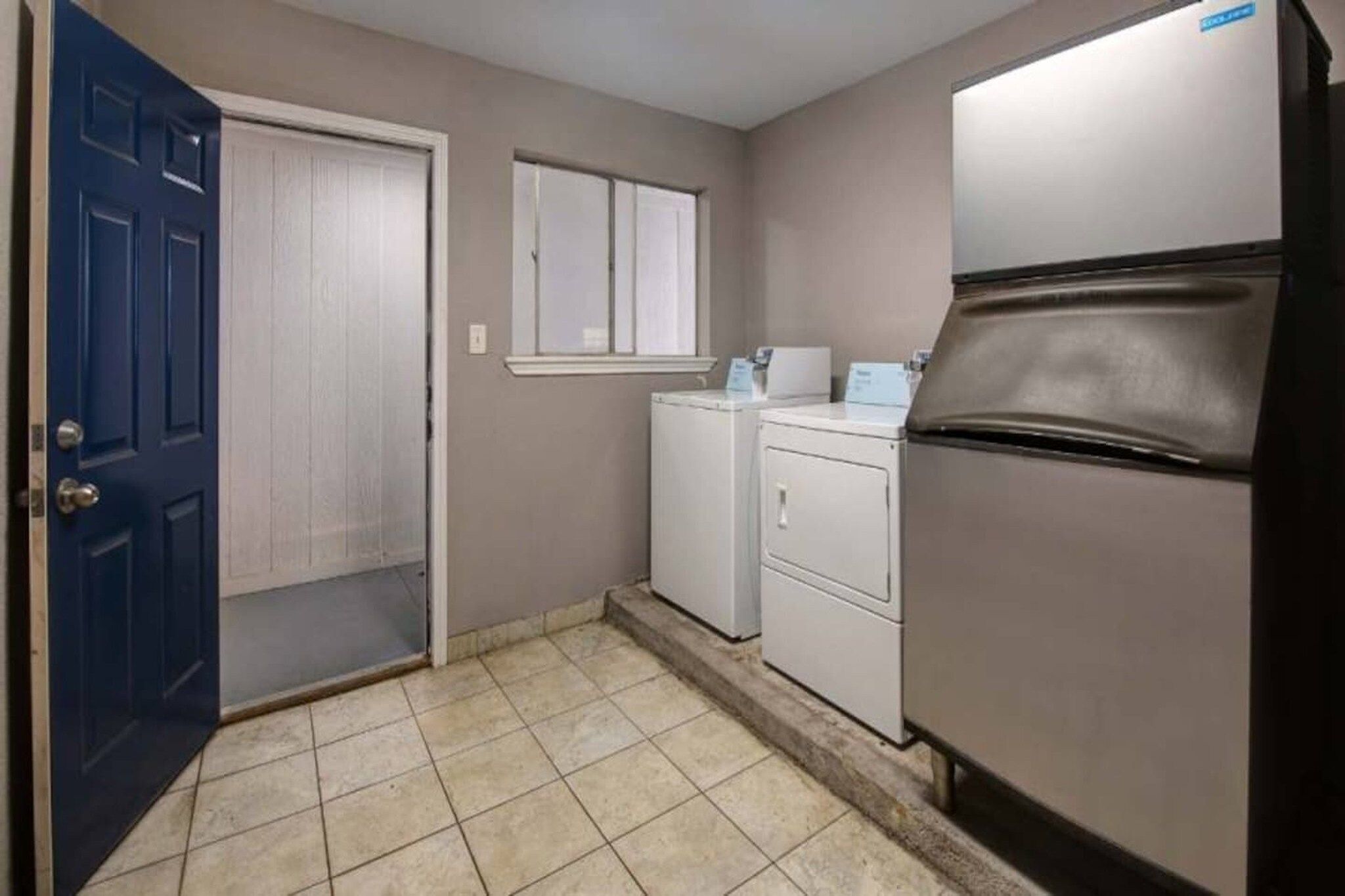 A laundry room with a blue door, a washing machine, a dryer, and a refrigerator.
