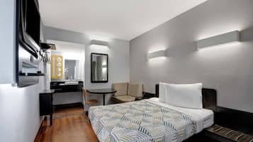 Een hotelkamer met een bed, een bureau, een stoel, een spiegel en een wandlamp.