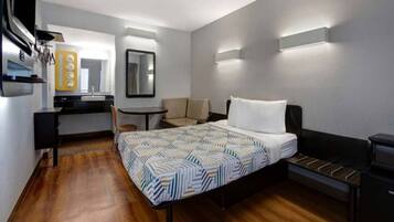 Ein Hotelzimmer mit Bett, Schreibtisch, Stuhl, kleinem Tisch und Spiegel.