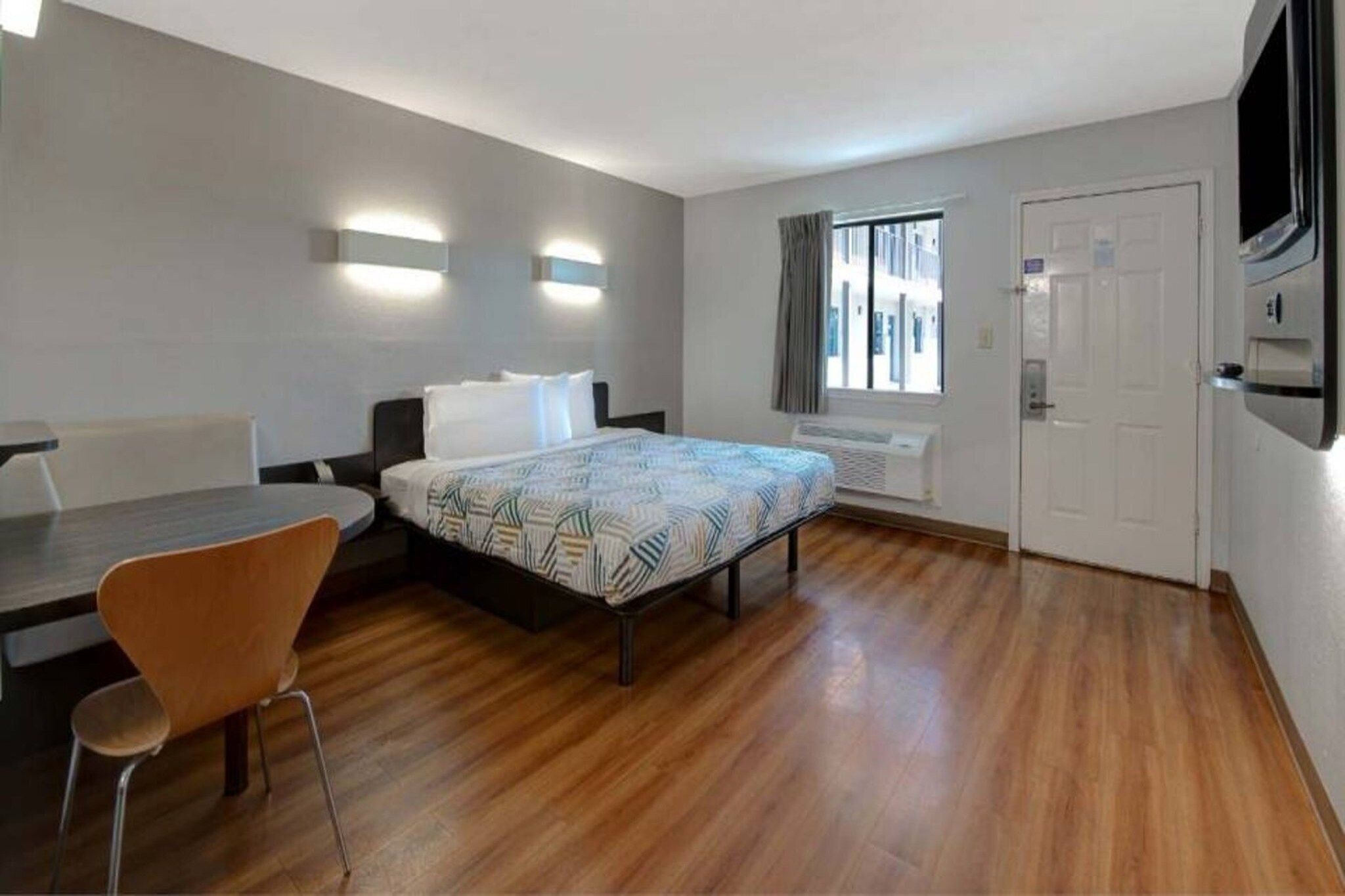 Ein Hotelzimmer mit Bett, Schreibtisch, Stuhl, Fernseher und einer Tür.