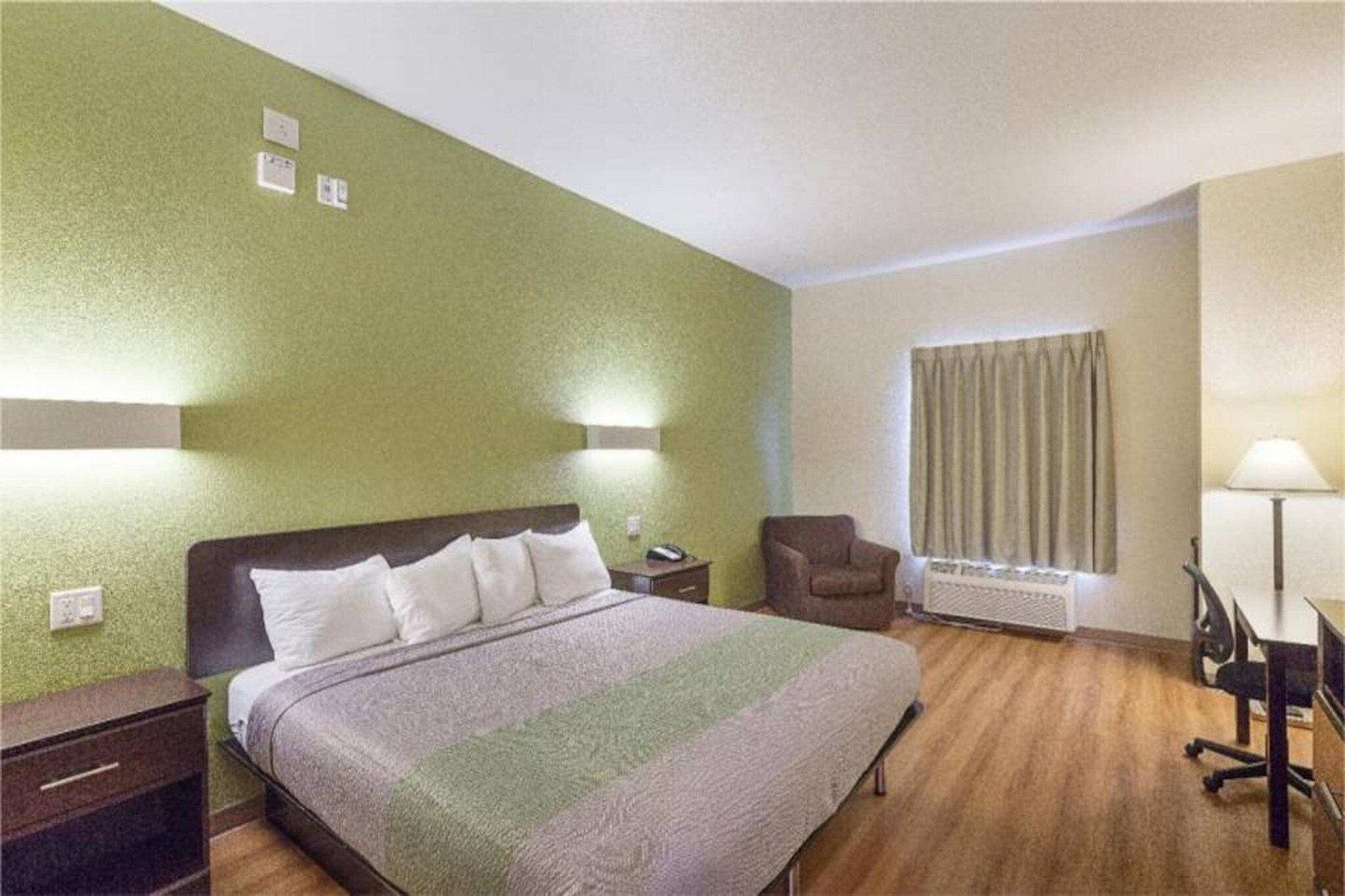 A hotel room with a bed, a desk, a chair, and a window with curtains.