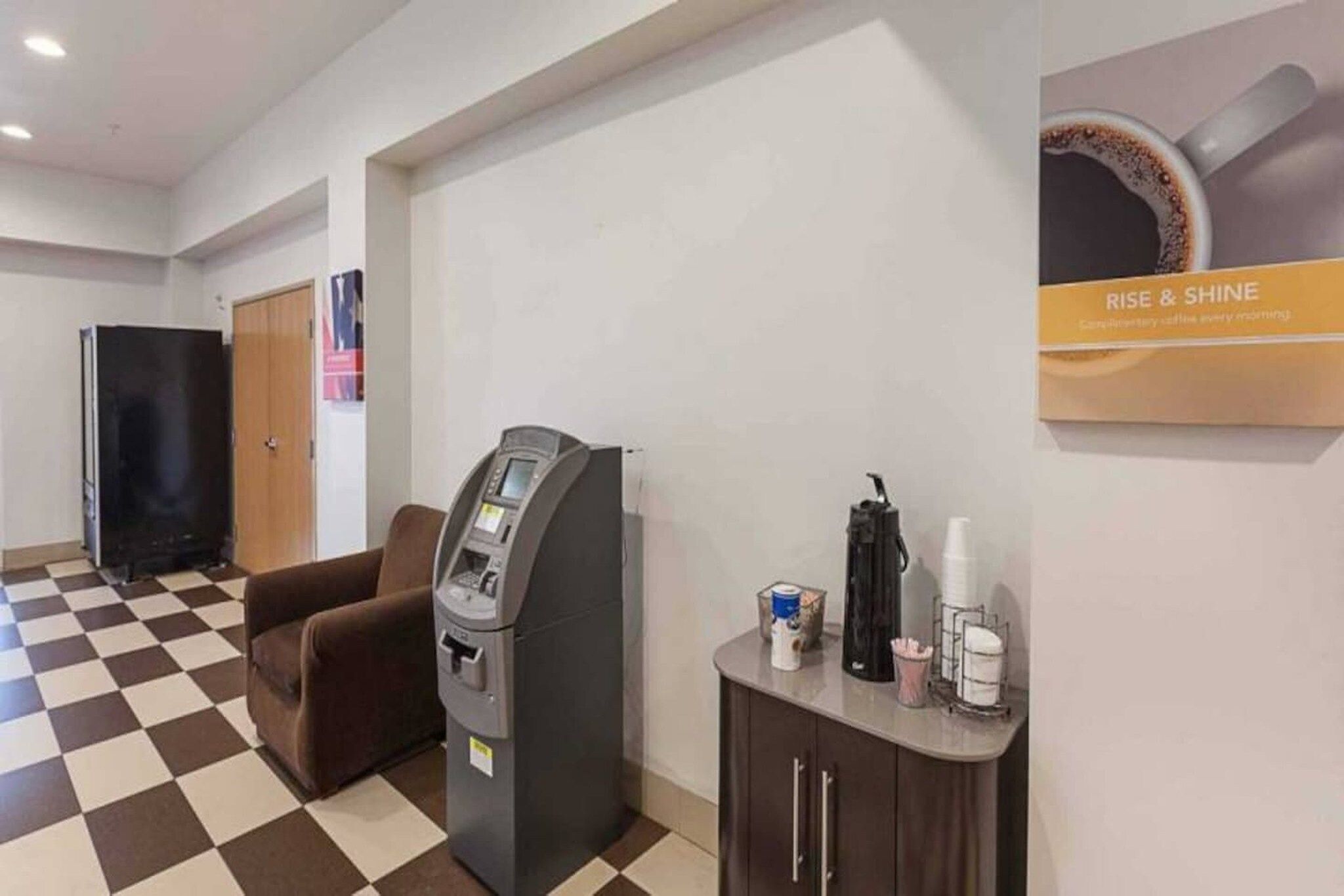A hotel lobby with a check-in kiosk, a seating area, and a coffee station.