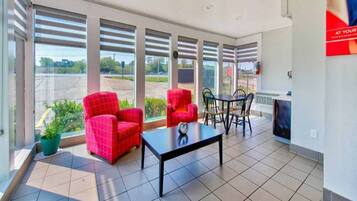 A modern room with large windows, a dining table, two red chairs, and a small potted plant.