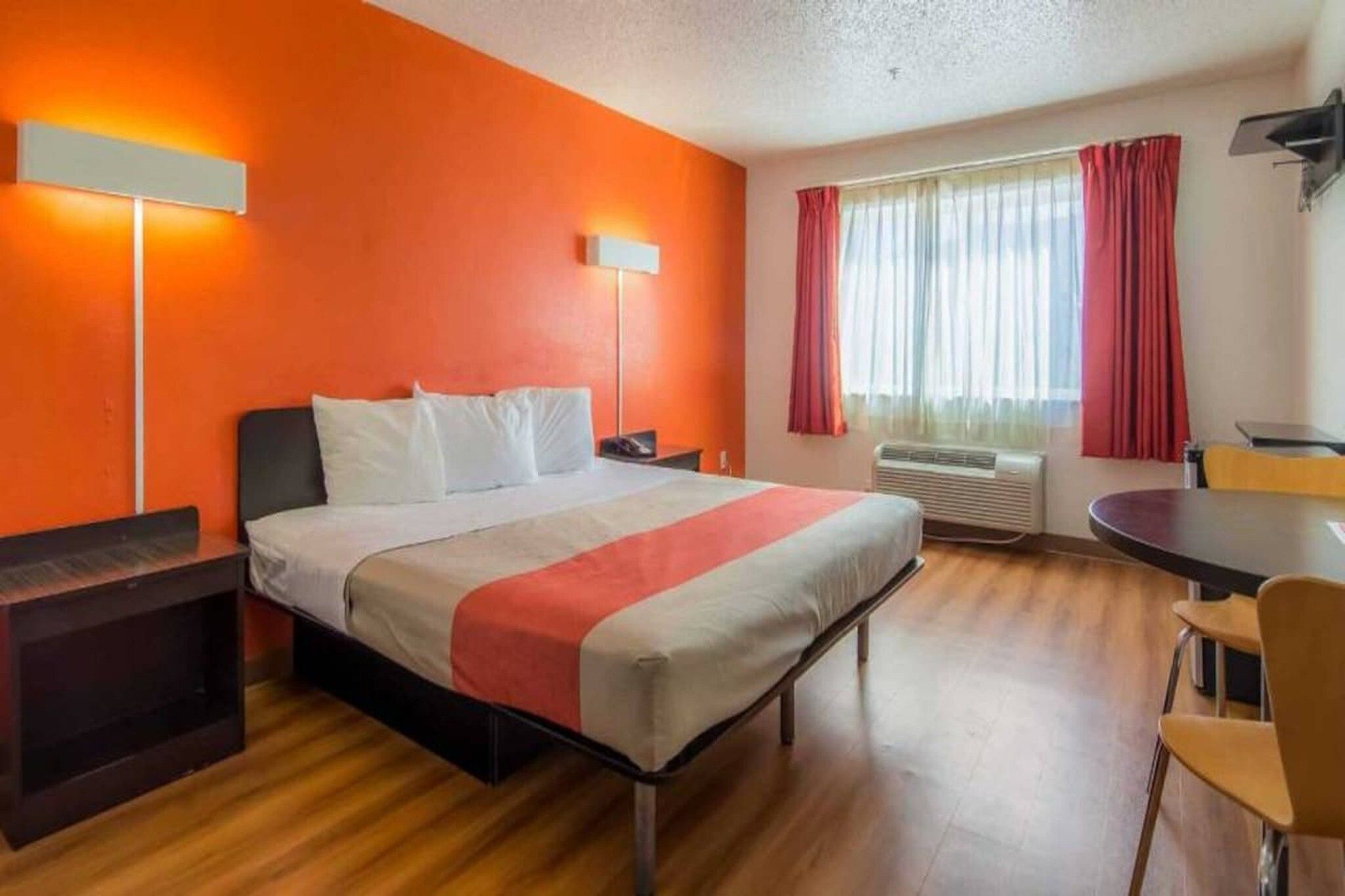 A hotel room with a bed, bedside tables, a desk, a chair, and a window with curtains.
