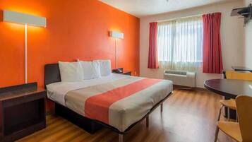 A hotel room with a bed, bedside tables, a desk, a chair, and a window with curtains.