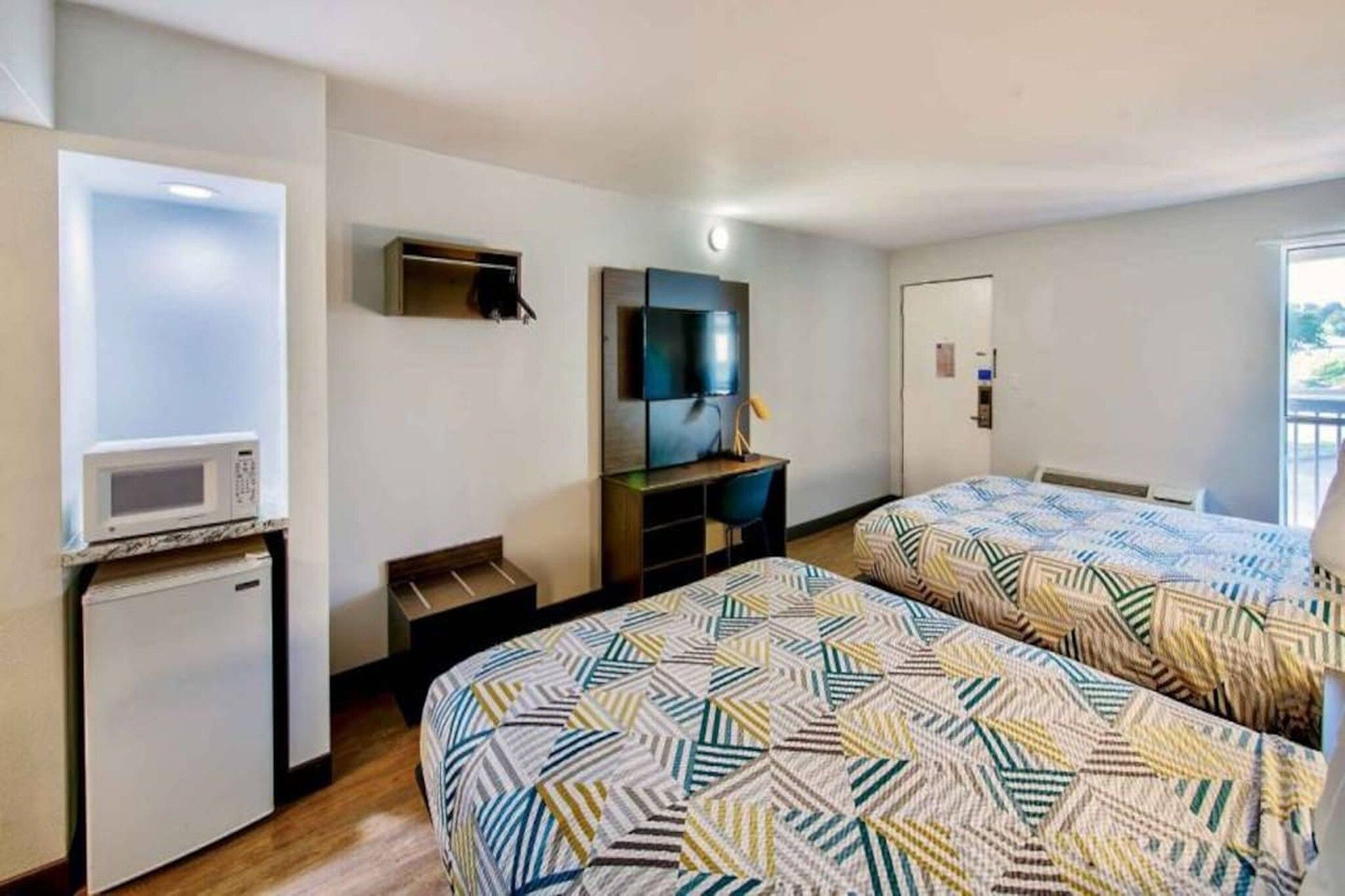 A hotel room with two beds, a TV, a microwave, and a small desk.