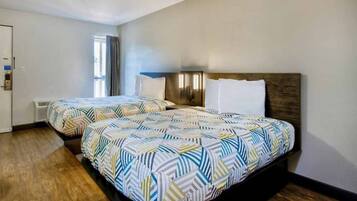 Une chambre d’hôtel avec deux lits, une fenêtre avec des rideaux, un climatiseur fixé au mur et une porte avec une poignée.