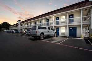 A motel with a parking lot, a white pickup truck, and multiple rooms with blue doors. - 1 Queen Bed | Non - Smoking (Dallas)