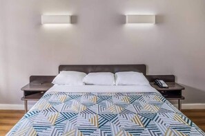 A hotel room with a bed, two bedside tables, and two wall-mounted lights. - 1 Queen Bed | Non - Smoking (Dallas)