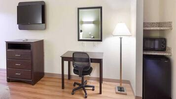 A hotel room with a desk, chair, dresser, lamp, and microwave.