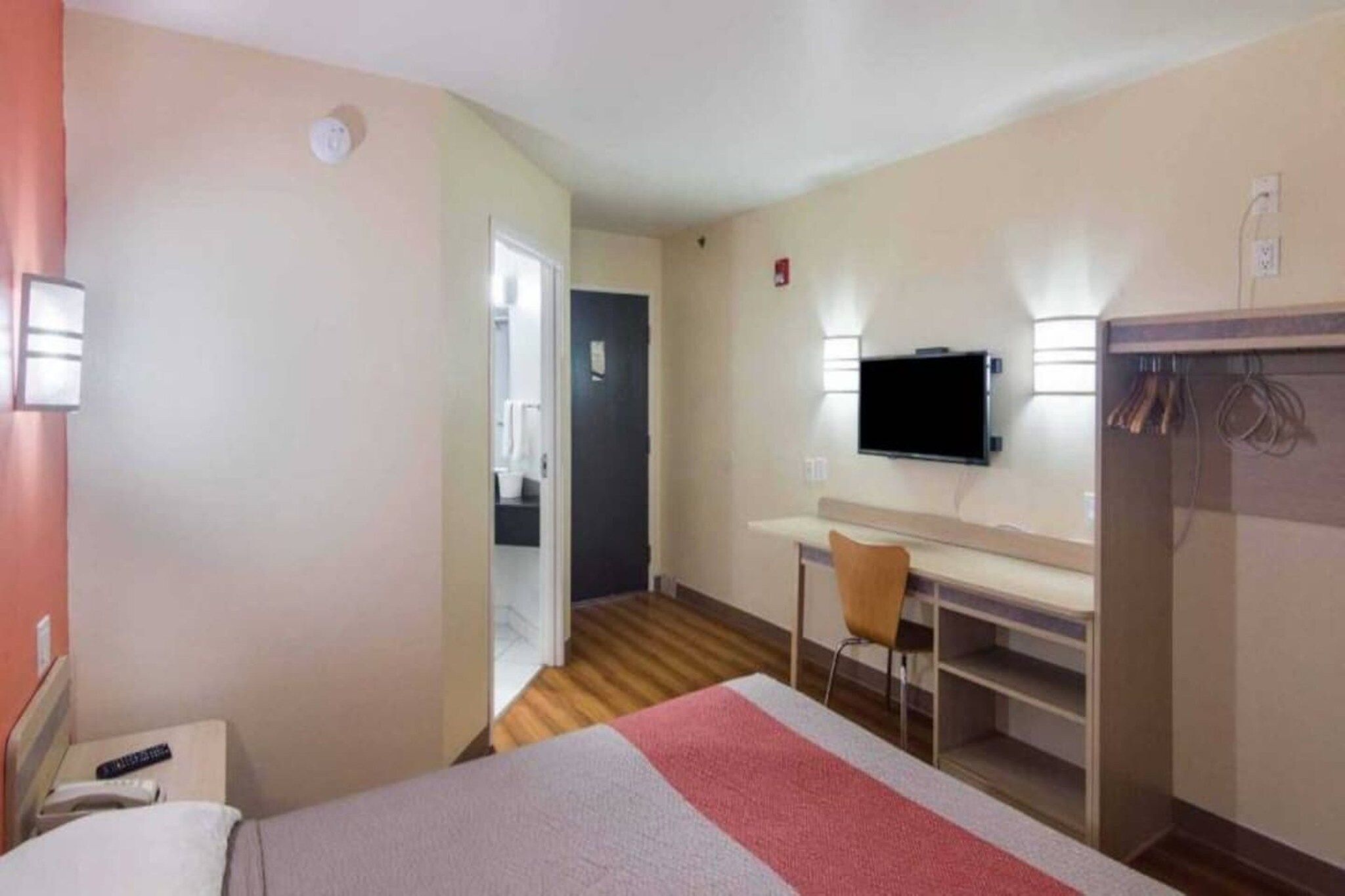A hotel room with a bed, a desk, a chair, a television, and a wardrobe.