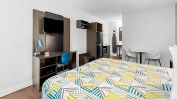 A hotel room with a bed, a desk, a chair, a TV, and a kitchenette.