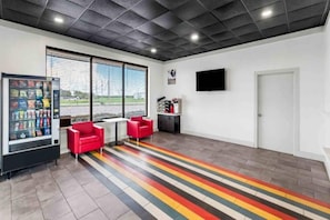 A modern interior with a vending machine, red chairs, a flat-screen TV, and a door. - 1 King Bed | Non-Smoking, Micfridge (Port Lavaca)