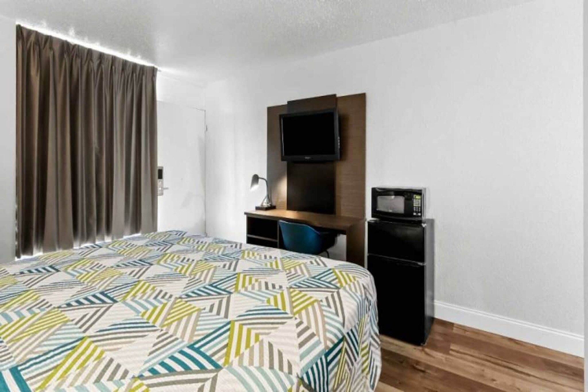 A hotel room with a bed, a desk, a television, and a refrigerator.