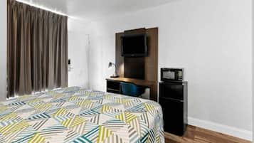A hotel room with a bed, a desk, a television, and a refrigerator.