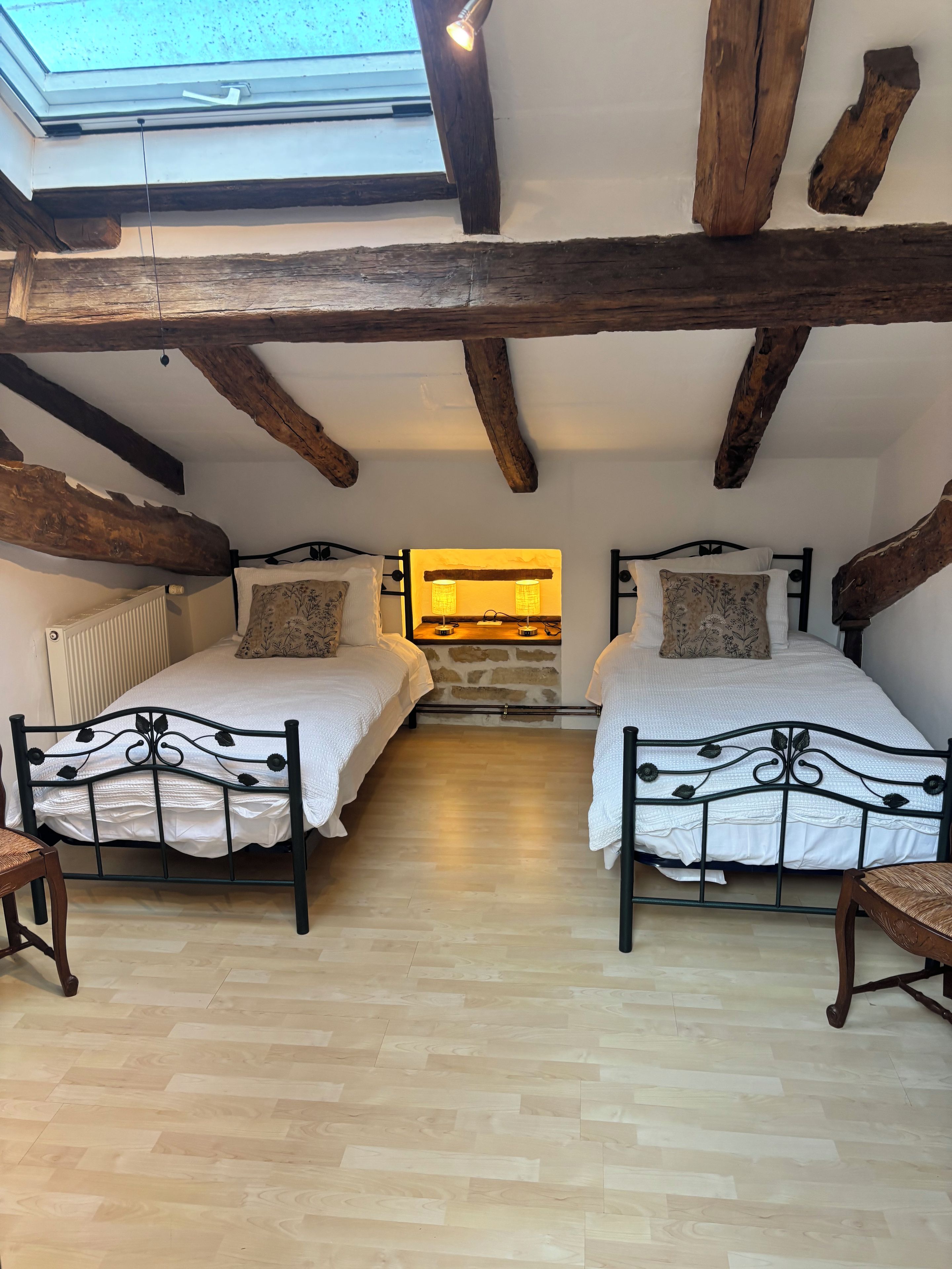 Een kamer met twee bedden, dakraam, houten balken en een stenen muur.